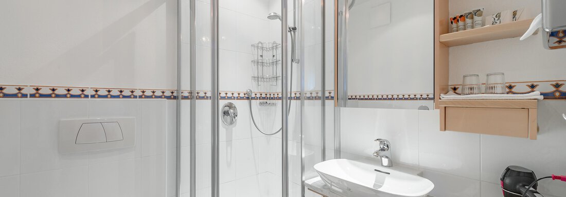 A modern bathroom with a shower cabin and a sink. There is also a shelf with various toiletries. - Villa Castelbell - Sölden
