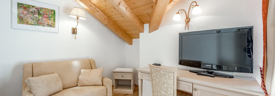 A cozy room with a modern sofa and a desk. On the wall hangs a television, and the wooden ceiling gives off a rustic charm. - Villa Castelbell - Sölden