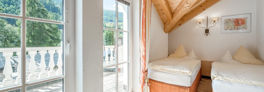 A bright room with two beds and a wooden ceiling. Large windows offer a view of the mountains and access to a balcony. - Villa Castelbell - Sölden