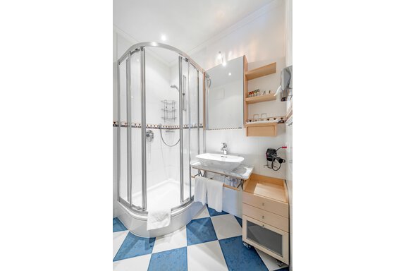 A modern bathroom with a shower cabin and a sink. The floor is designed with blue and white tiles. - Villa Castelbell - Sölden