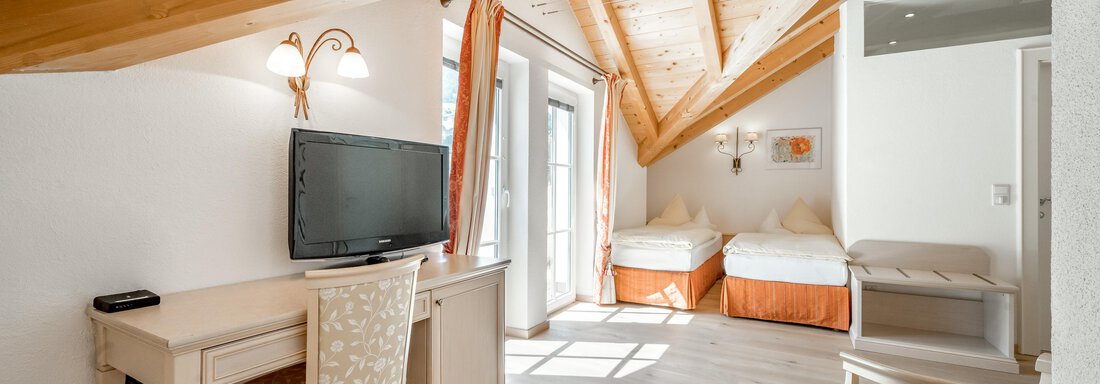 A cozy bedroom with a wooden ceiling and large windows. There is a desk, a television, and two single beds. - Villa Castelbell - Sölden
