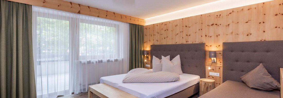A modern hotel room with wooden paneling and two beds. Large windows provide plenty of daylight and a pleasant atmosphere. - Vizensn Living - Sölden