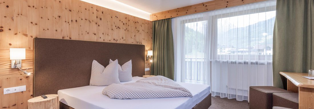 A cozy hotel room with a large bed and wooden paneling. The windows provide a view of the surrounding landscape. - Vizensn Living - Sölden