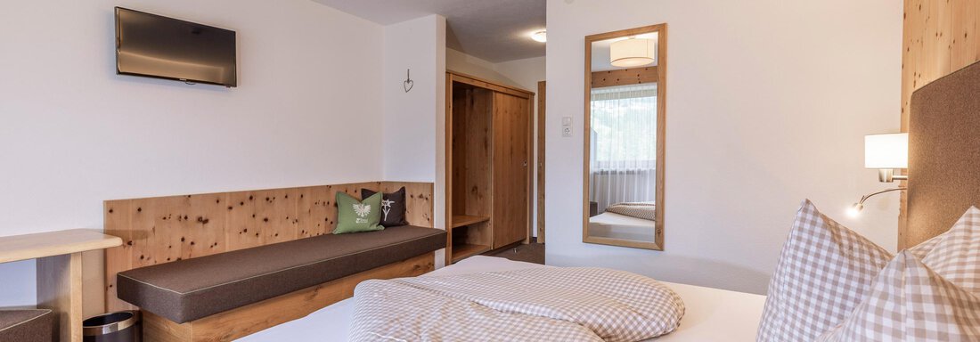 A cozy hotel room with a large bed and pillows. There is a television and a wooden seating area. - Vizensn Living - Sölden