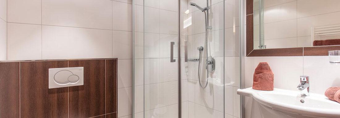 A modern bathroom with a glass shower, a sink, and a toilet. The walls are tiled in light colors, and the design is elegant and functional. - Vizensn Living - Sölden