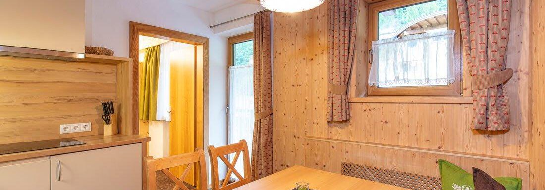 A cozy kitchen with wooden furniture and a dining table. The windows provide plenty of daylight, and the walls are designed with wooden paneling. - Vizensn Living - Sölden
