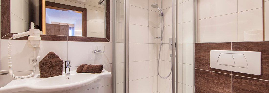 A modern bathroom with a glass shower and a sink. The walls are designed with light tiles and wood effect. - Vizensn Living - Sölden