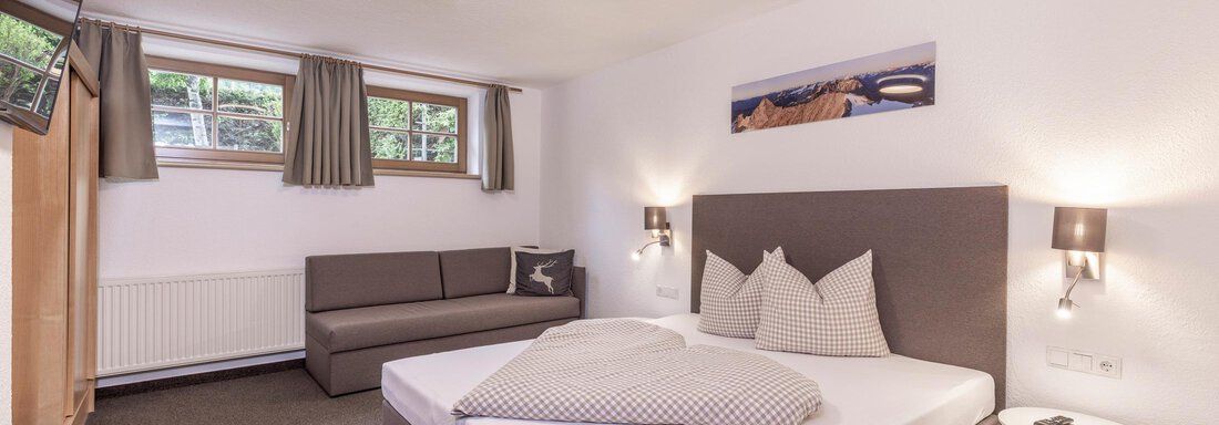 A modern bedroom with a large bed and a cozy couch. There are windows with curtains and a television on the wall. - Vizensn Living - Sölden