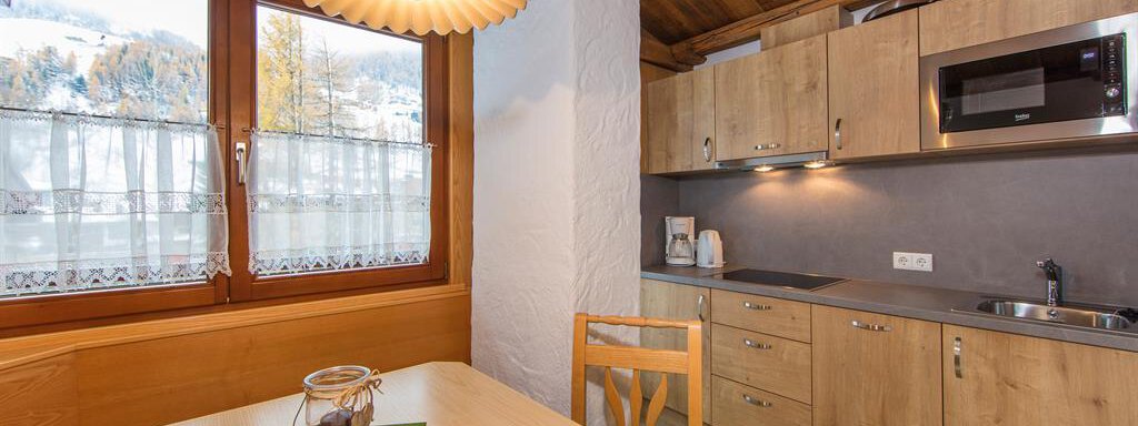 A modern kitchenette with wooden cabinets and a dining area. Large windows provide a view of the mountains. - Vizensn Living - Sölden