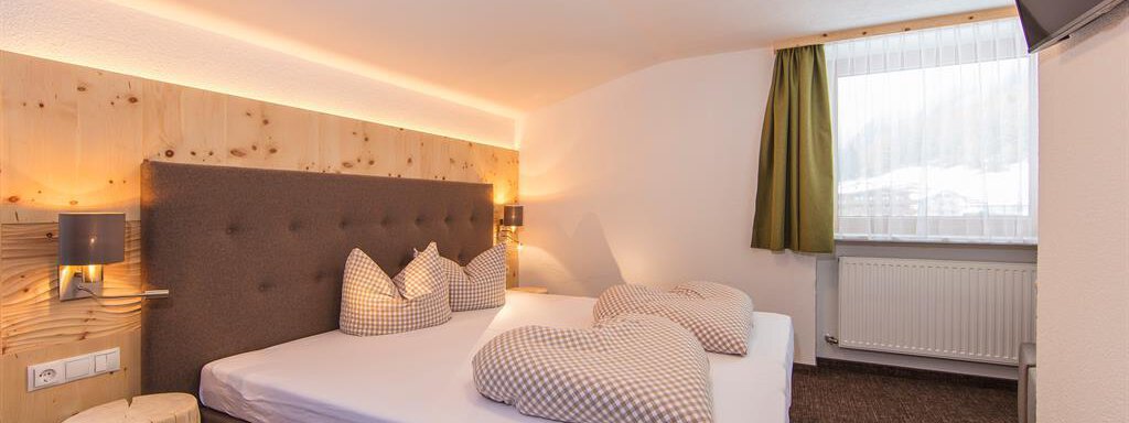 A cozy bedroom with a large bed and stylish pillows. The warm wood and green tones create an inviting atmosphere. - Vizensn Living - Sölden