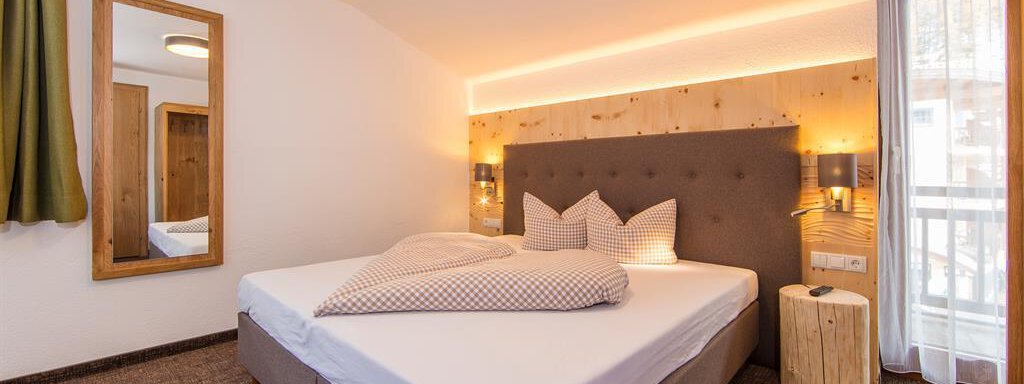 A cozy bedroom with a large bed and modern wood details.  
Large windows let in plenty of light and create an inviting atmosphere. - Vizensn Living - Sölden