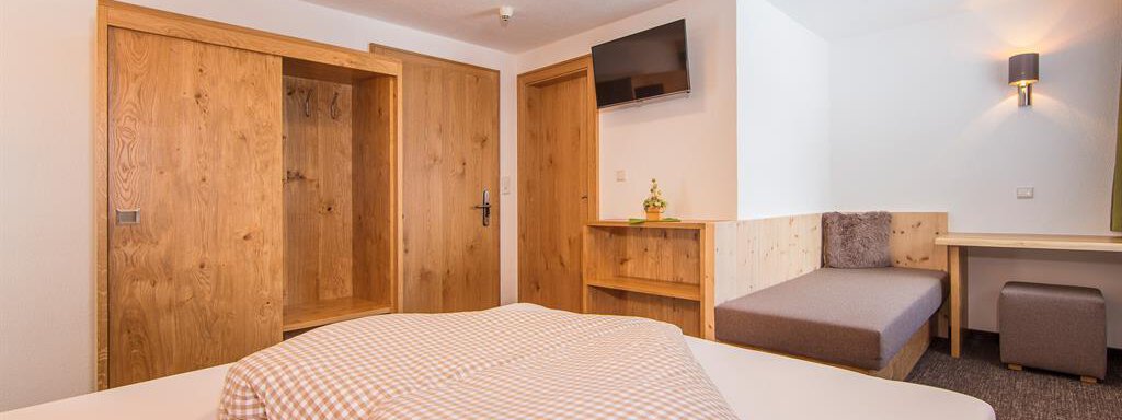 A cozy room with a double bed and wooden details. There is a television and a sitting area with an upholstered bench. - Vizensn Living - Sölden