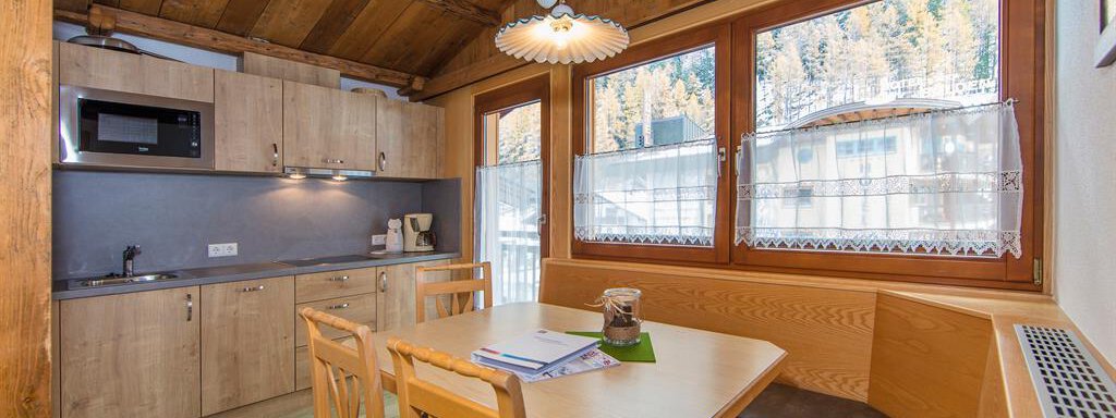 A cozy kitchen with a wooden ceiling and a dining area. Large windows offer a view of the surrounding landscape. - Vizensn Living - Sölden