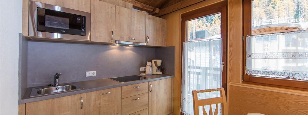 A cozy kitchen area with wooden cabinets and modern appliances. Generous windows provide plenty of daylight. - Vizensn Living - Sölden
