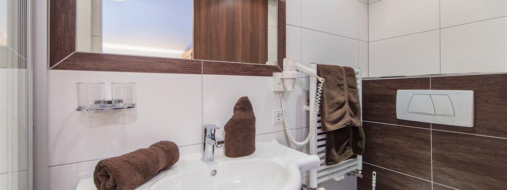 A modern bathroom with a sink, towels, and a bustling shower cabin. The walls are mostly tiled, providing a clean, elegant ambiance. - Vizensn Living - Sölden