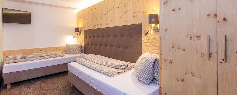 A modern bedroom with two beds and a wood panel. The walls are light and the lighting creates a cozy atmosphere. - Vizensn Living - Sölden