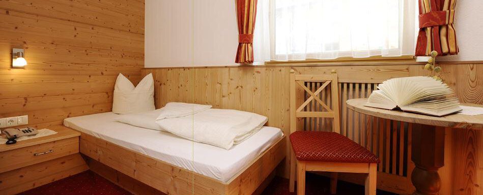 A cozy room with wooden walls and a single bed. An open book is on the table and a chair is next to it. - Vizensn Living - Sölden