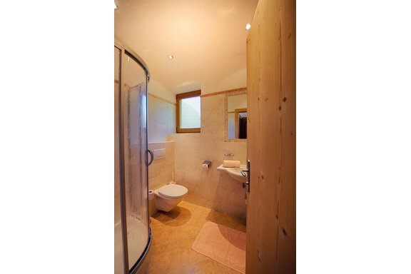 A modern bathroom with a shower, toilet, and sink. It has bright tiles and natural lighting from a window. - Vizensn Living - Sölden