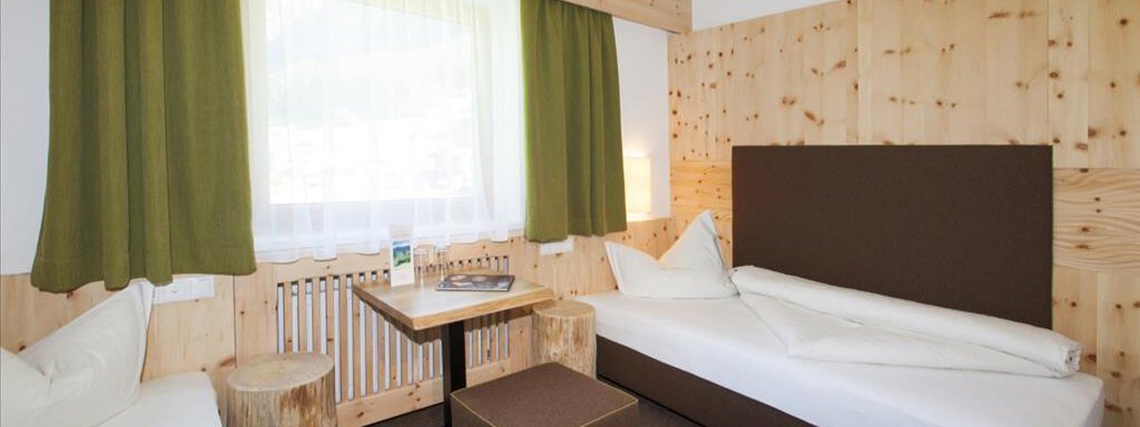 A modern room with wooden walls and large windows. The furnishings consist of two beds, a small table, and a cozy seating area. - Vizensn Living - Sölden