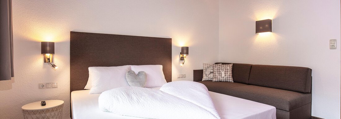 A comfortable hotel room with a large bed and a cozy couch. The walls are light and friendly, with atmospheric lighting. - Vizensn Living - Sölden