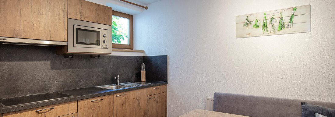 A modern kitchen with wooden cabinets and a dining area. The room is bright and inviting with a window that lets in natural light. - Vizensn Living - Sölden