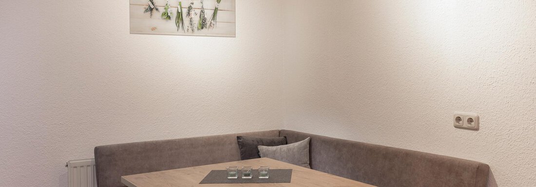 A cozy dining area with a rectangular wooden table and an upholstered bench. A decorative picture hangs on the wall. - Vizensn Living - Sölden
