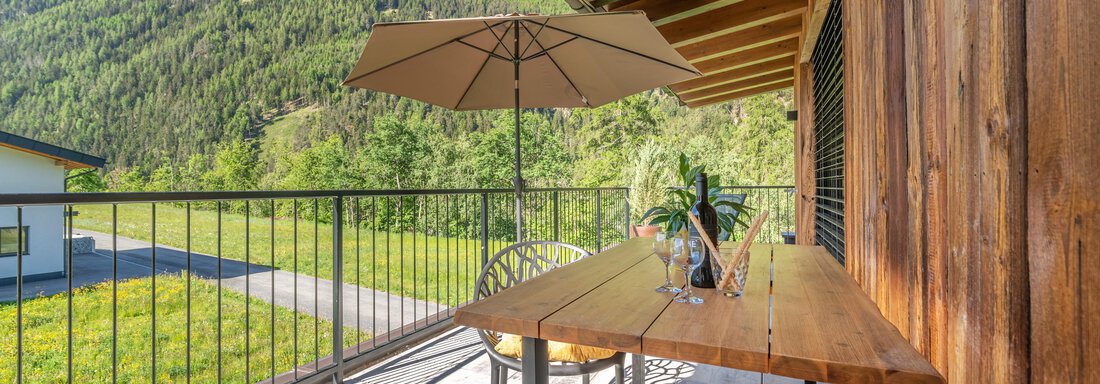 Eine gemütliche Terrasse mit einem Tisch und Stühlen. Im Hintergrund sieht man grüne Berge und einen klaren blauen Himmel. - Apart Dorhoam - Umhausen