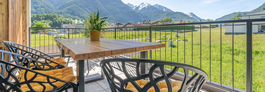 Ein gemütlicher Balkon mit modernen Stühlen und einem Tisch. Im Hintergrund sind grüne Wiesen und Berge unter einem klaren blauen Himmel zu sehen. - Apart Dorhoam - Umhausen