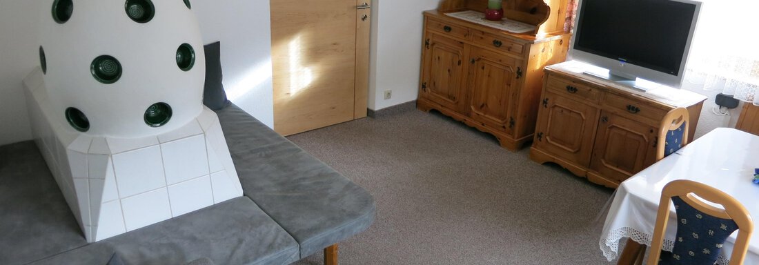 A cozy living room with a gray couch and a wooden cabinet. The television is next to a table that is covered with a white tablecloth. - Apart Martina - Umhausen
