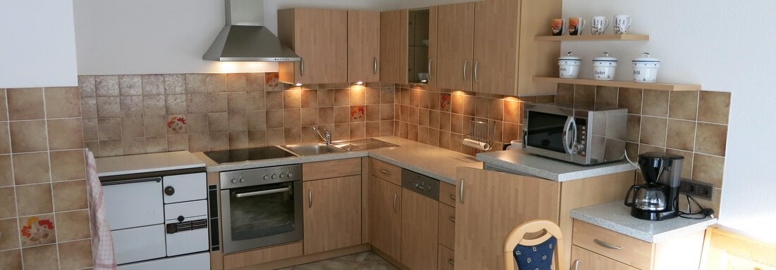 A modern kitchen with wooden cabinets and a sink. There is a dining table and various kitchen appliances. - Apart Martina - Umhausen
