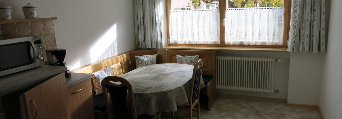 A bright kitchen with a round dining table and chairs. Large windows provide daylight and a view outside. - Apart Martina - Umhausen