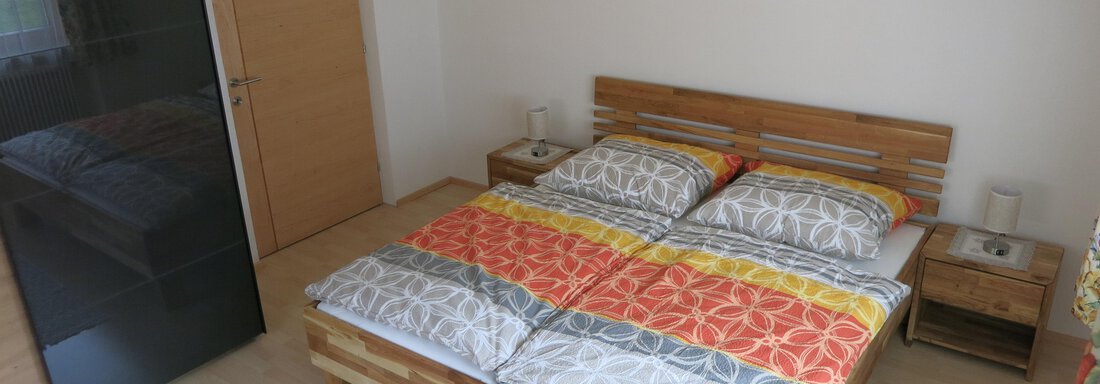 A modern bedroom with a double bed and colorful bedding. The walls are light and there are some pictures as well as a wardrobe. - Apart Martina - Umhausen