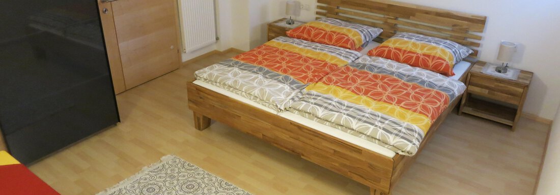 A cozy bedroom with a wooden bed and colorful blankets. The room has a bright wooden floor and a simple, modern decor. - Apart Martina - Umhausen