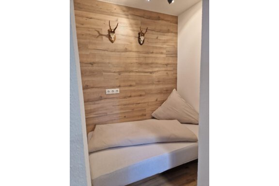 Eine gemütliche Ecke mit einem schlichten Sofa und großen Kissen. Die Holzvertäfelung an der Wand verleiht dem Raum eine warme Atmosphäre. - Apart Waldnest - Umhausen
