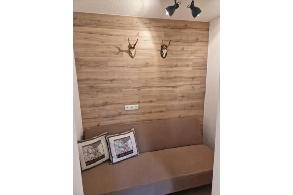 Ein gemütlicher Raum mit einer Holzverkleidung und zwei Geweihköpfen an der Wand. Ein beiges Sofa und dekorative Kissen verleihen dem Raum eine einladende Atmosphäre. - Apart Waldnest - Umhausen