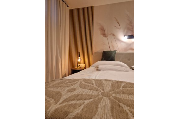 Ein gemütliches Schlafzimmer mit einem großen Bett und einer stilvollen Bettwäsche. Im Hintergrund sind eine Lampe und dekorative Wände zu sehen. - Apart Waldnest - Umhausen