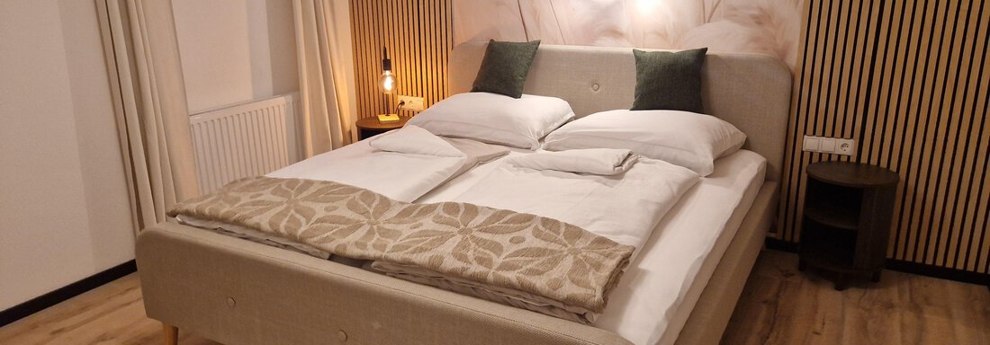 Ein modernes Schlafzimmer mit einem großen Bett und gemütlichen Kissen. Die warmen Holz- und Beigetöne schaffen eine entspannte Atmosphäre. - Apart Waldnest - Umhausen