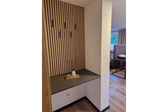 Ein moderner Eingangsbereich mit einer Holzpaneelwand und vier Haken. Auf der Ablage befindet sich eine Vase und eine kleine Dekoration. - Apart Waldnest - Umhausen