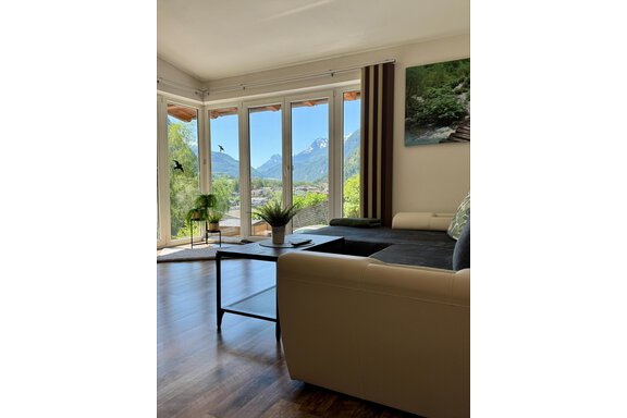 Ein gemütliches Wohnzimmer mit einem Blick auf die Berge. Große Fenster lassen viel Licht herein und bieten einen schönen Ausblick auf die Natur. - Appartement Bergglück - Umhausen