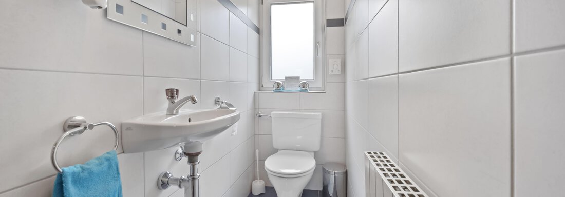 A modern bathroom with white tiles and a small window. It contains a sink, a toilet, and a radiator. - Biancas Ferienwohnung im Haus Roswitha - Umhausen