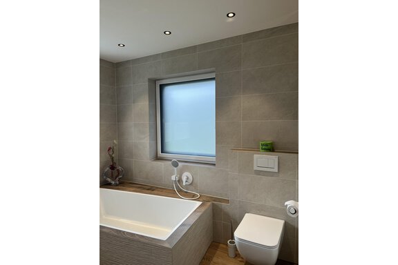 Ein modernes Badezimmer mit einer Badewanne und einem WC. Der Raum hat große Fenster und helle Wände. - BLANKA'S Apart Auszeit - Umhausen