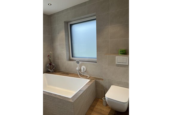Ein modernes Badezimmer mit einer Badewanne und einer Toilette. Die Wände sind in neutralen Grau-Tönen gehalten und es gibt ein Fenster mit Sichtschutz. - BLANKA'S Apart Auszeit - Umhausen
