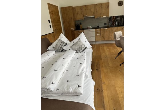Ein gemütliches Zimmer mit einem großen Bett und einer modernen Küchenzeile. Der Holzfußboden sorgt für eine warme Atmosphäre. - BLANKA'S Apart Auszeit - Umhausen