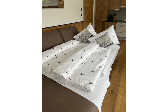 Ein gemütliches Bett mit weißen Bettdecken und Kissen, die ein elegantes Design haben. Im Hintergrund ist eine moderne Küche zu sehen. - BLANKA'S Apart Auszeit - Umhausen