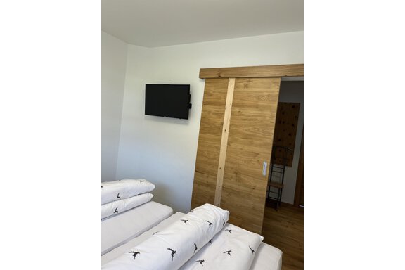 Ein modernes Schlafzimmer mit einem Flachbildfernseher an der Wand. Die Möbel sind aus hellem Holz und die Bettwäsche ist ordentlich aufgeschichtet. - BLANKA'S Apart Auszeit - Umhausen
