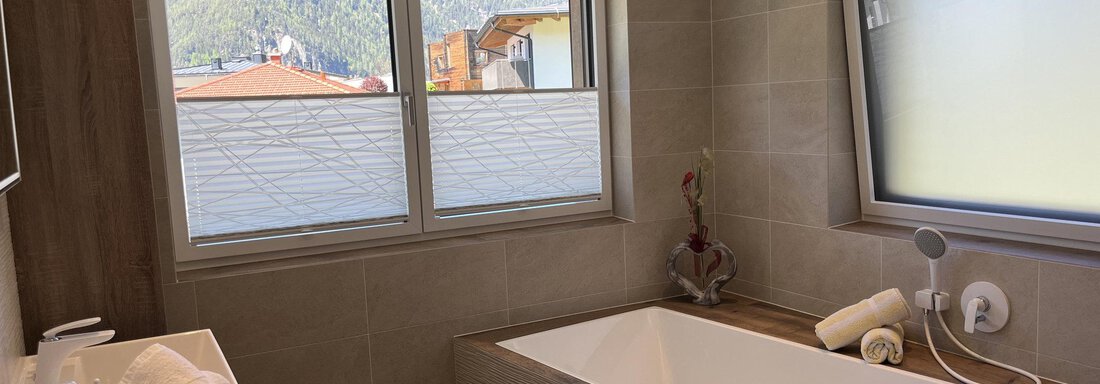 Ein modernes Badezimmer mit einer Badewanne und Fensterblick auf die Umgebung. Die Wände sind in neutralen Tönen gehalten, was eine entspannende Atmosphäre schafft. - BLANKA'S Apart Auszeit - Umhausen