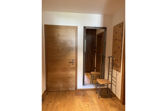 Ein heller Eingangsbereich mit einem Holzfußboden. Auf der linken Seite befindet sich eine Holz-Tür, daneben ein Spiegel und ein Stuhl. - BLANKA'S Apart Auszeit - Umhausen