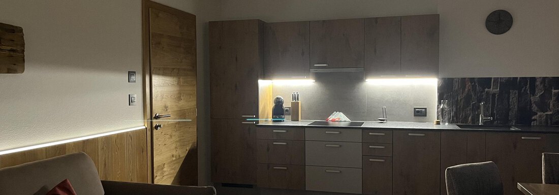 Eine moderne Küche mit Holzmöbeln und sanfter Beleuchtung. Im Vordergrund steht ein gemütliches Sofa. - BLANKA'S Apart Auszeit - Umhausen
