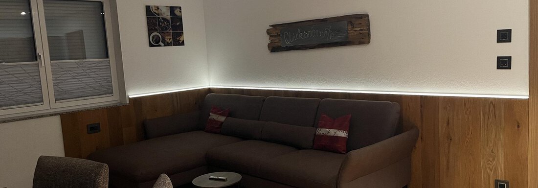 Ein gemütlicher Wohnraum mit einem modernen Sofa und einem Tisch. Die Wände sind aus Holz, und die Beleuchtung sorgt für eine angenehme Atmosphäre. - BLANKA'S Apart Auszeit - Umhausen