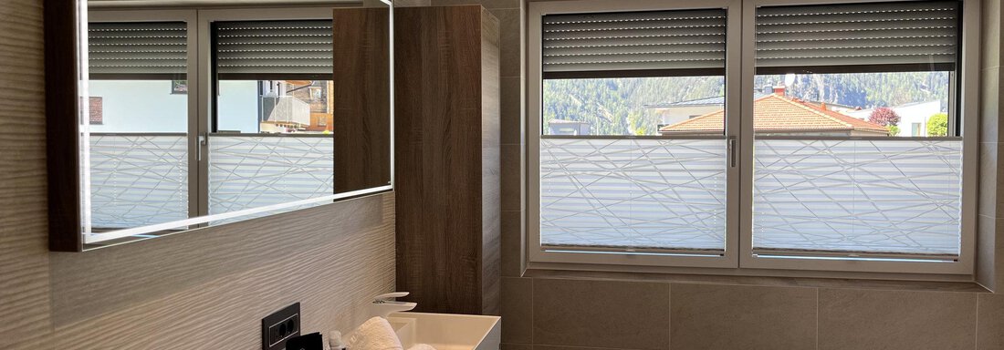 Ein modernes Badezimmer mit einem großen Spiegel und einem Waschbecken. Die Fenster bieten einen Blick nach draußen und sorgen für viel Tageslicht. - BLANKA'S Apart Auszeit - Umhausen